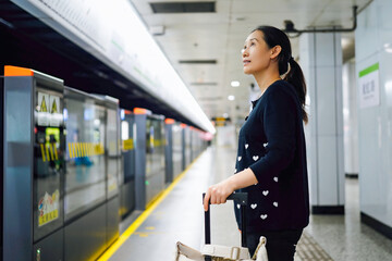 Obraz premium Woman Waiting at Subway Platform with Luggage in Urban Setting