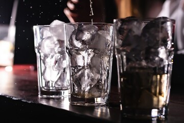 Close-up of the hands of a bartender pouring an alcoholic drink to make a cocktail in a glass glass