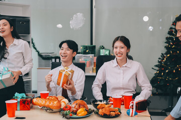 full length view of a group of business team wearing red Santa hat and exchange gift box together in the office for Christmas.