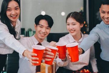 full length view of a group of business team wearing red Santa hat and exchange gift box together in the office for Christmas.