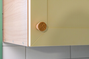 Wooden handle attached to yellow sleek kitchen cabinet with a simple design. Solid oak cabinet knob close up view