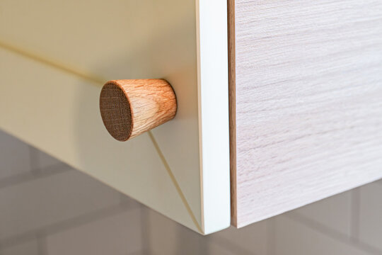 Wooden handle attached to yellow sleek kitchen cabinet with a simple design. Solid oak cabinet knob close up view