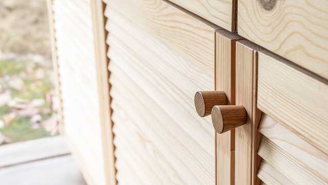Wooden louvered doors with wooden knob handles close-up. Louvered doors of outdoor kitchen are made from light pine wood with natural grain pattern
