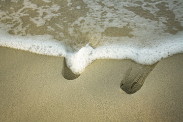 Human footprints with white foamy wave on sandy beach. Summer vacation concept
