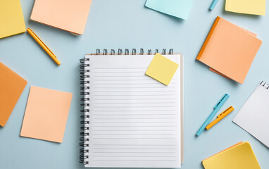 Flat lay of a blank notebook and colorful sticky notes on a light blue background.