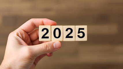 A hand is holding up a block of wood that says 2025 on it