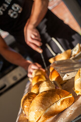 A person is skillfully cutting into fresh, warm baguettes on a rustic wooden board, illuminated by natural light