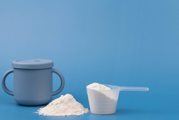 Baby formula powder in a measuring scoop with baby bottle on blue background. Clean, soft setup with purity, simplicity. Infant nutrition, baby care, and wholesome ingredients Minimalistic concept. 