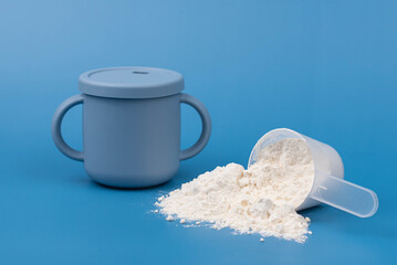 Baby formula powder in a measuring scoop with baby bottle on blue background. Clean, soft setup with purity, simplicity. Infant nutrition, baby care, and wholesome ingredients Minimalistic concept. 