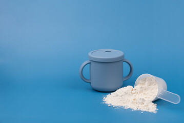 Baby formula powder in a measuring scoop with baby bottle on blue background. Clean, soft setup with purity, simplicity. Infant nutrition, baby care, and wholesome ingredients Minimalistic concept. 