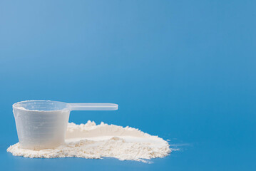 White protein powder, collagen supplement, or baby formula in measuring scoop on blue background. Concept of health, wellness, child food nutrition, fitness, skincare, and childcare. 