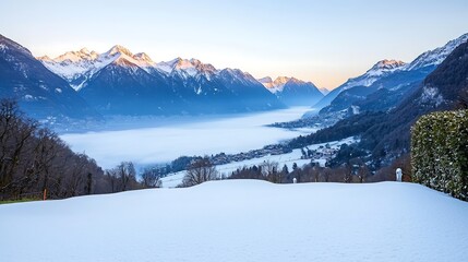 A panoramic view of a winter sunrise illuminating a mountain range, where the first light of day highlights the snow-capped peaks. The foreground features a tranquil valley blanketed in fresh snow,