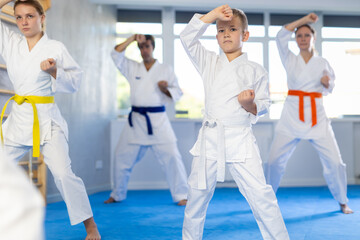 Boy with his family in kimonos and colored belts practicing karate punch block during group martial arts lesson in gym, accompanied by trainer © JackF