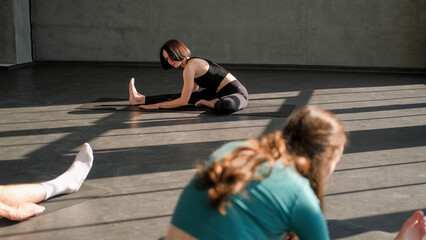 Gymnastic training. Stretch exercise. Fit woman yoga instructor teaching group flexibility workout fitness class recreation practice on mat in gym sport studio indoors.