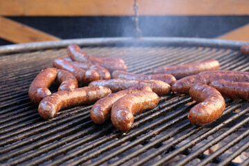 Close-up of large beef sausages being grilled on an open grill with a grate. Delicious food for a large group of people.