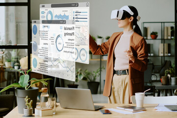 Young Asian female developer wearing VR headset testing virtual application at work in leading IT company office with biophilic design