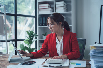 Focused Businesswoman:  A professional woman wearing a red blazer intently works on her tablet in a...
