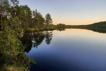 Tranquil lake reflecting forest under evening sky.