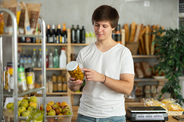 Young male shopper chooses olive in jar in grocery store