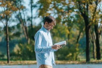 Man Reads as He Walks in a Tranquil Park Setting on a Bright Day