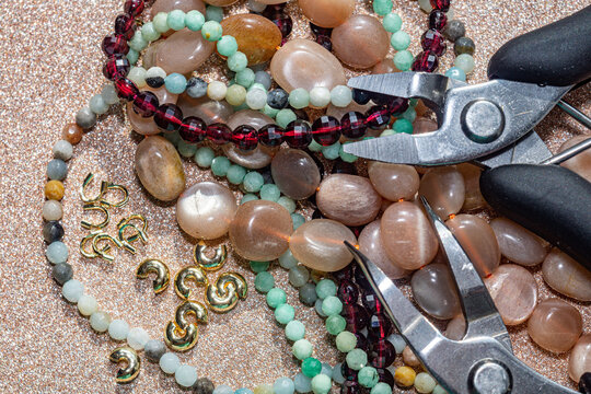 Close up photo featuring a collection of beads made from natural stones, gold-plated beads, and tools for crafting jewelry. Image for jewelry designers, crafters, for web banners.