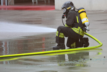 firefighter with a hose spraying foam extinguishing agent and an oxygen tank