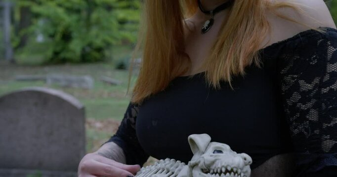Beautiful Witch petting a toy bone dog in the cemetery. Tilt up Close up slow motion.