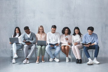 Multiracial young group of people sitting in line and waiting for job interview, talking to each...
