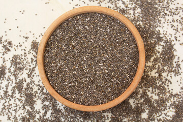 Chia seeds in a bowl with some scattered on the ground, showcasing their raw, natural texture. Ideal for health, nutrition, and superfood content.