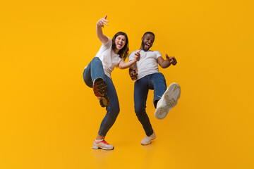 Yo. Positive interracial couple fooling together, having fun and laughing at camera over yellow studio background, low angle view