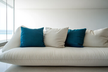 Elegant white sofa with teal cushions in minimalist coastal living room overlooking the ocean