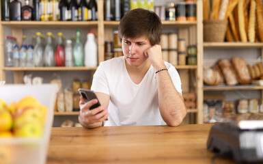 Supermarket food department manager carefully reads messages on a smartphone screen