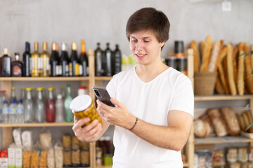 Young man scans a qr code on a can of olives in a supermarket. European makes purchases through an online application on his phone