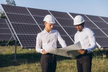 Engineers in Hard Hats Reviewing Blueprints at Solar Panel Farm under Clear Sky