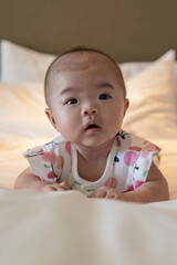 Adorable infant lying on a bed, surrounded by scattered red rose petals, displaying a joyful smile