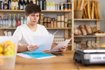 Young female seller examines documents at counter in grocery store