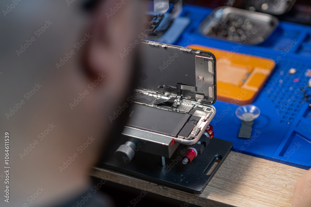 Poster a technician meticulously replaces a smartphone battery in a well-equipped workshop with various too