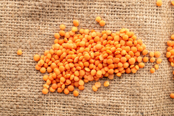 Raw red lentils on jute cloth, macro, top view.