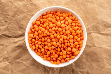 Raw red lentils in ceramic dish on kraft paper, macro, top view.