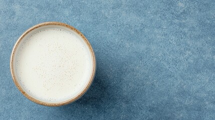 Bowl of creamy milk on textured blue background, evoking freshness and simplicity. Perfect for culinary or beverage themes