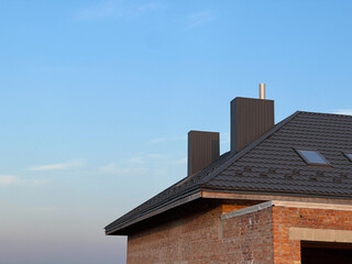 Two chimneys made of metal profile on one roof. Chimneys on the roof made of metal tiles.