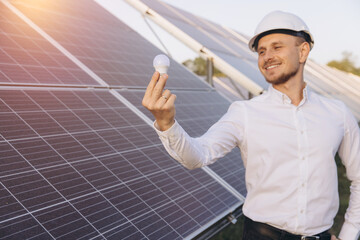 Smiling Engineer Holding LED Bulb Near Solar Panels