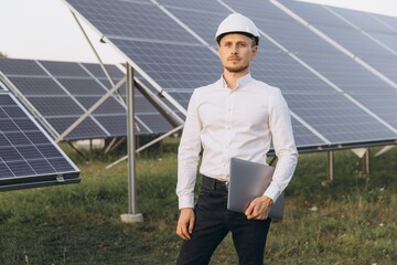 Engineer Standing Confidently at Solar Panel Farm With Laptop