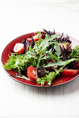 Salad with fresh tomatoes and arugula on a bright wooden background. Close up. Copy space.	