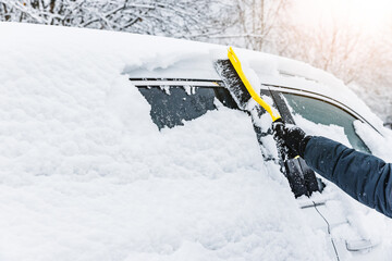 Man cleaning car from snow with yellow brush in winter time. Removing snow from car windows.