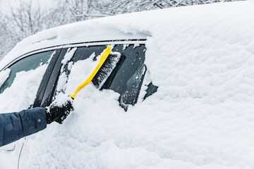 Man cleaning car from snow with yellow brush in winter time. Removing snow from car windows.