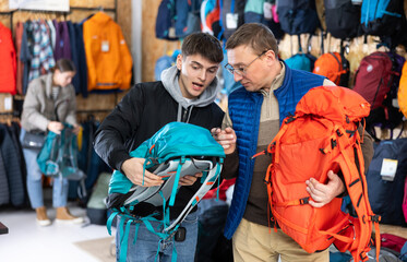 Father and son choose a backpack for hike together in a store that sells sports equipment