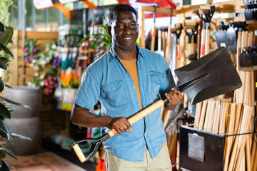 Portrait of african american man choosing shovel in gardening market