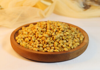 A wooden bowl containing fried soybeans, with a brown cloth decorated background