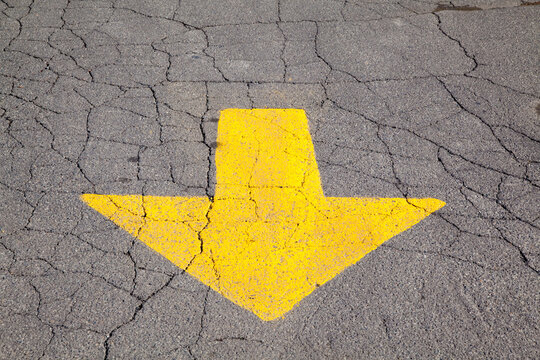 High angle close up of a yellow arrow on cracked tarmac.